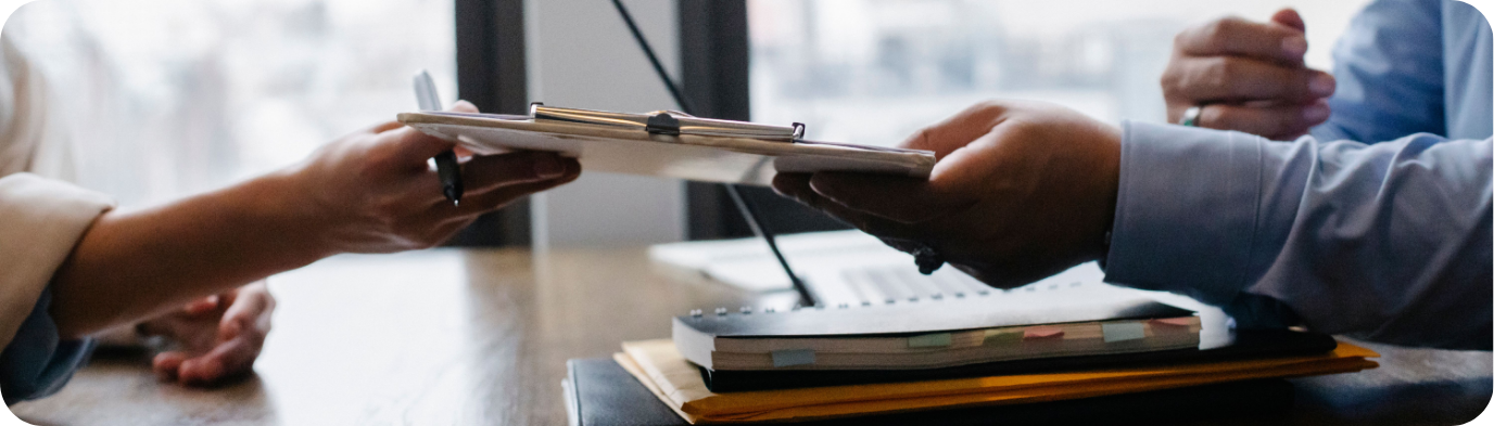 Hands exchanging documents during a professional meeting in an office environment.